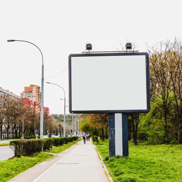Pusta, biała tablica reklamowa (billboard) na poboczu drogi miejskiej.