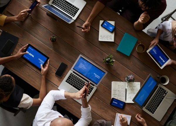 Grupa osób siedząca przy stole z laptopami i tabletami.